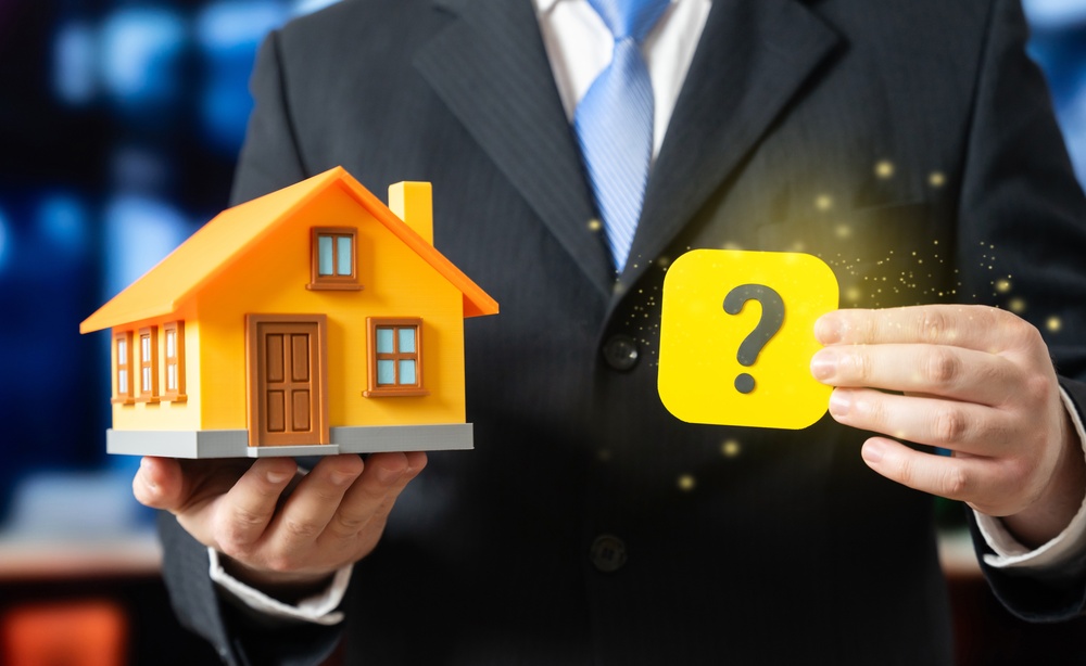 Photo of a man holding a miniature house in one hand and a question mark in the other, representing questions about the new regulations for the Future Homes Standard (FHS).