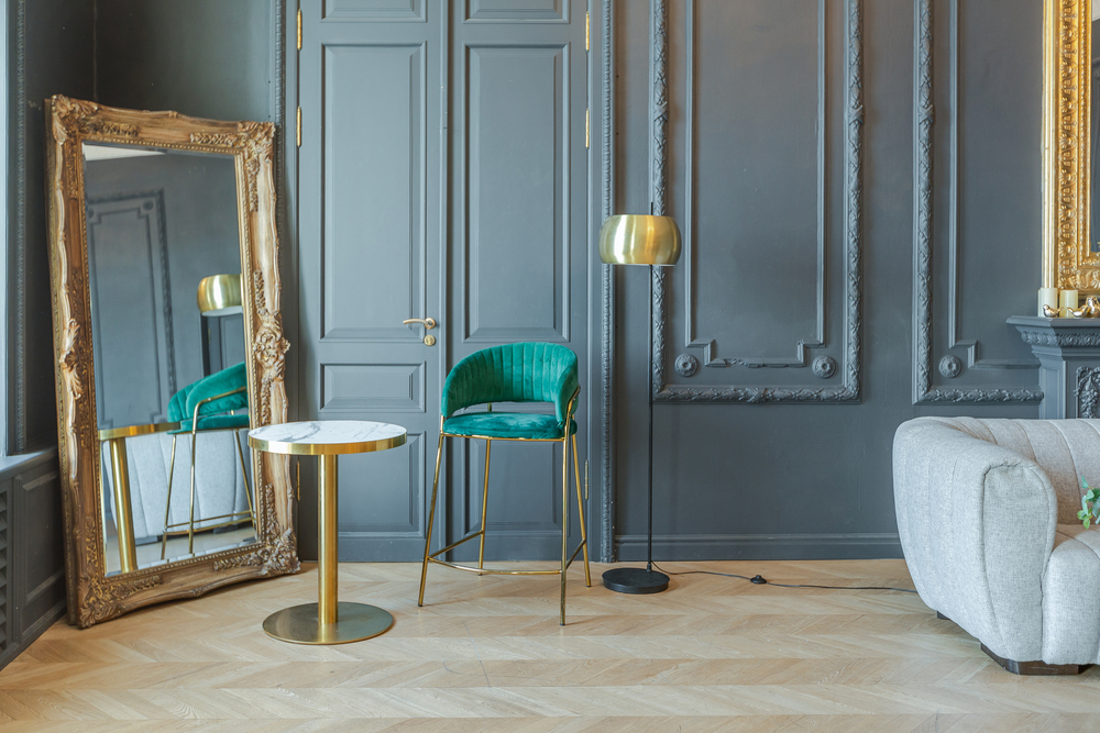 Classic panelled room with dark grey walls, ornate gold floor mirror, and a modern emerald green chair.