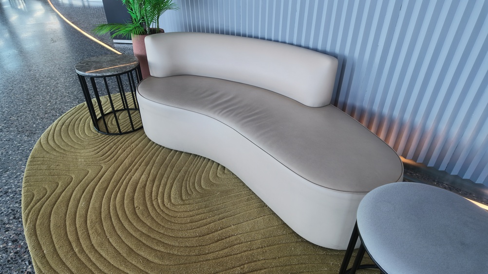 Curved minimalist sofa on a rippled olive green rug next to a fluted wall.