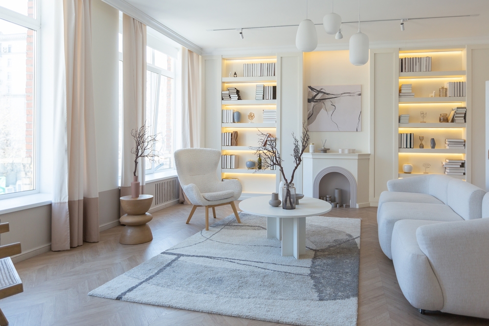 Monochromatic living room with warm neutrals, illuminated built-in bookshelves, and minimalist furniture.